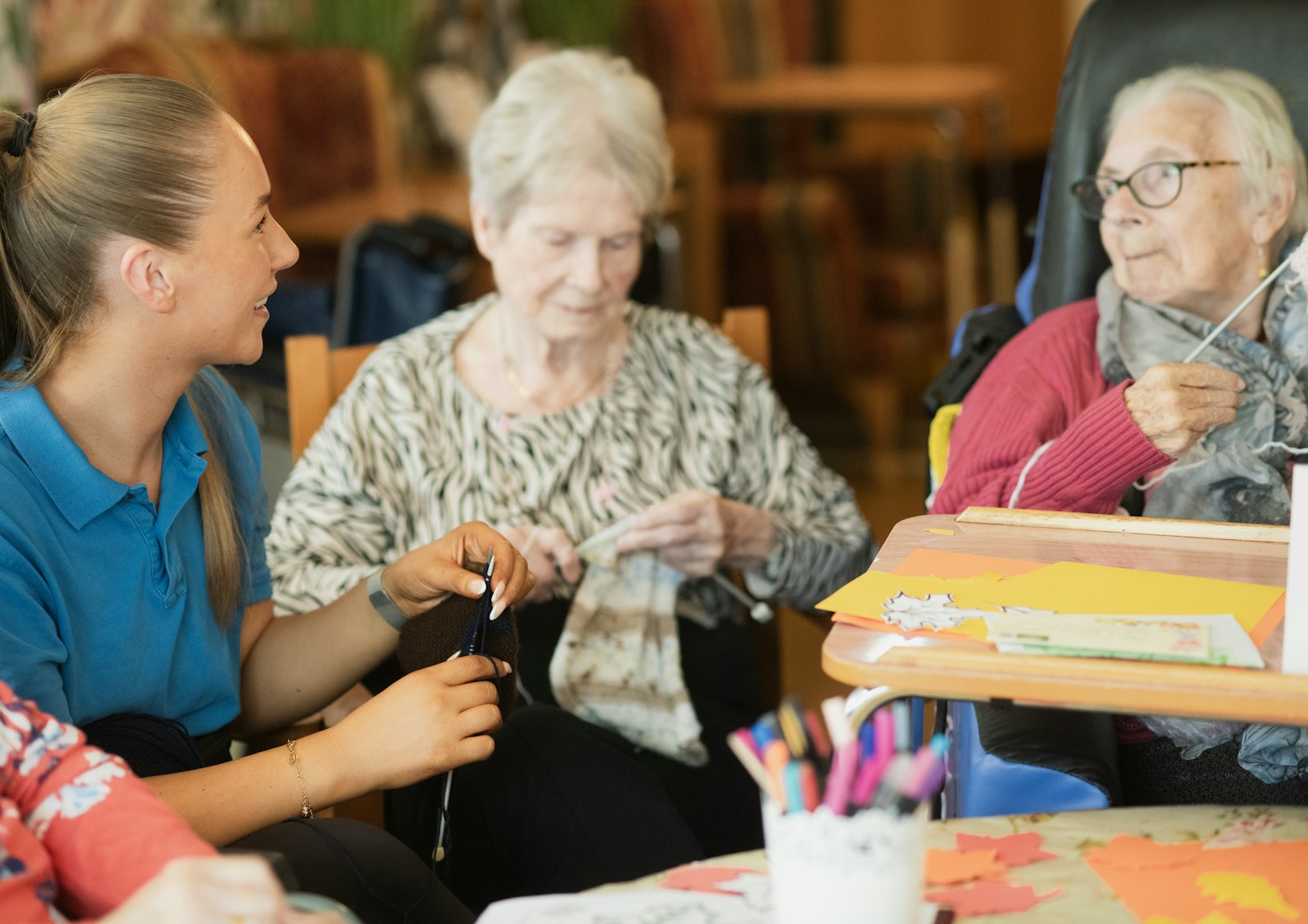 Residents working on knitting and paper crafts at a table with a staff member in a senior living community.